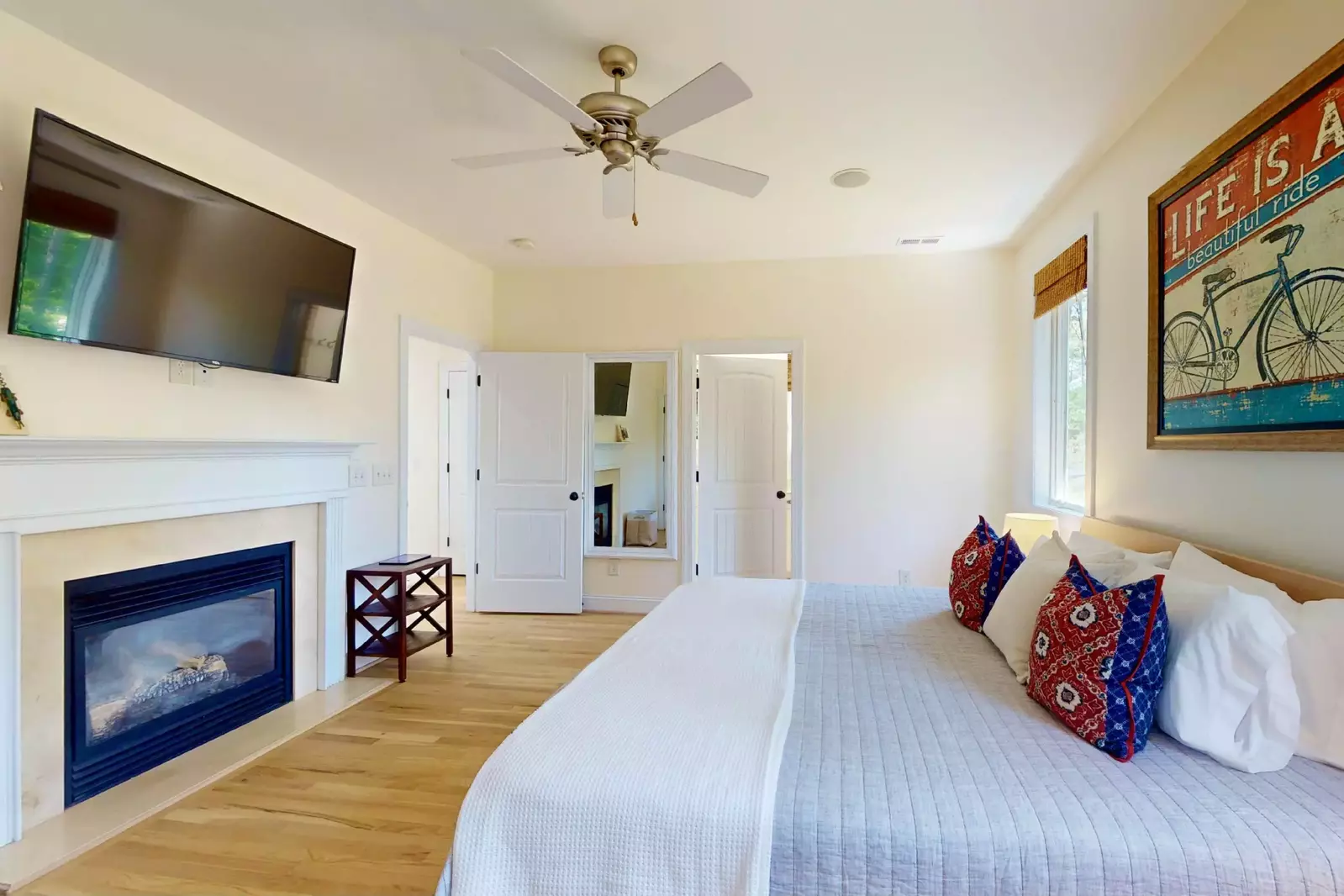 The bedroom has a king bed, wall mounted smart tv and a fireplace